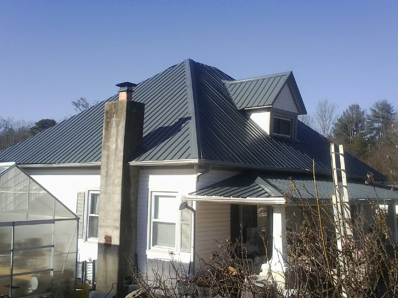 Dark blue standing seam metal roof on a white farmhouse with dormer — Slate & Tile Roof Repair by Roofing Brothers in Ellisburg