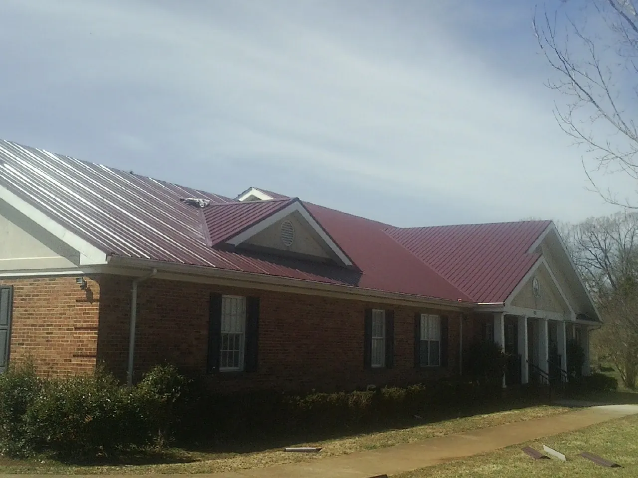 Red metal roof with gabled entries on a long brick building, from a Hail Damage Roof Repair job in Ellisburg