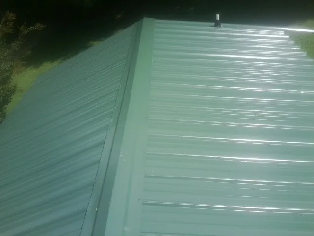 New green metal panels meeting at the ridge of a roof — Flat Roof Repair work by our crew in Ellisburg