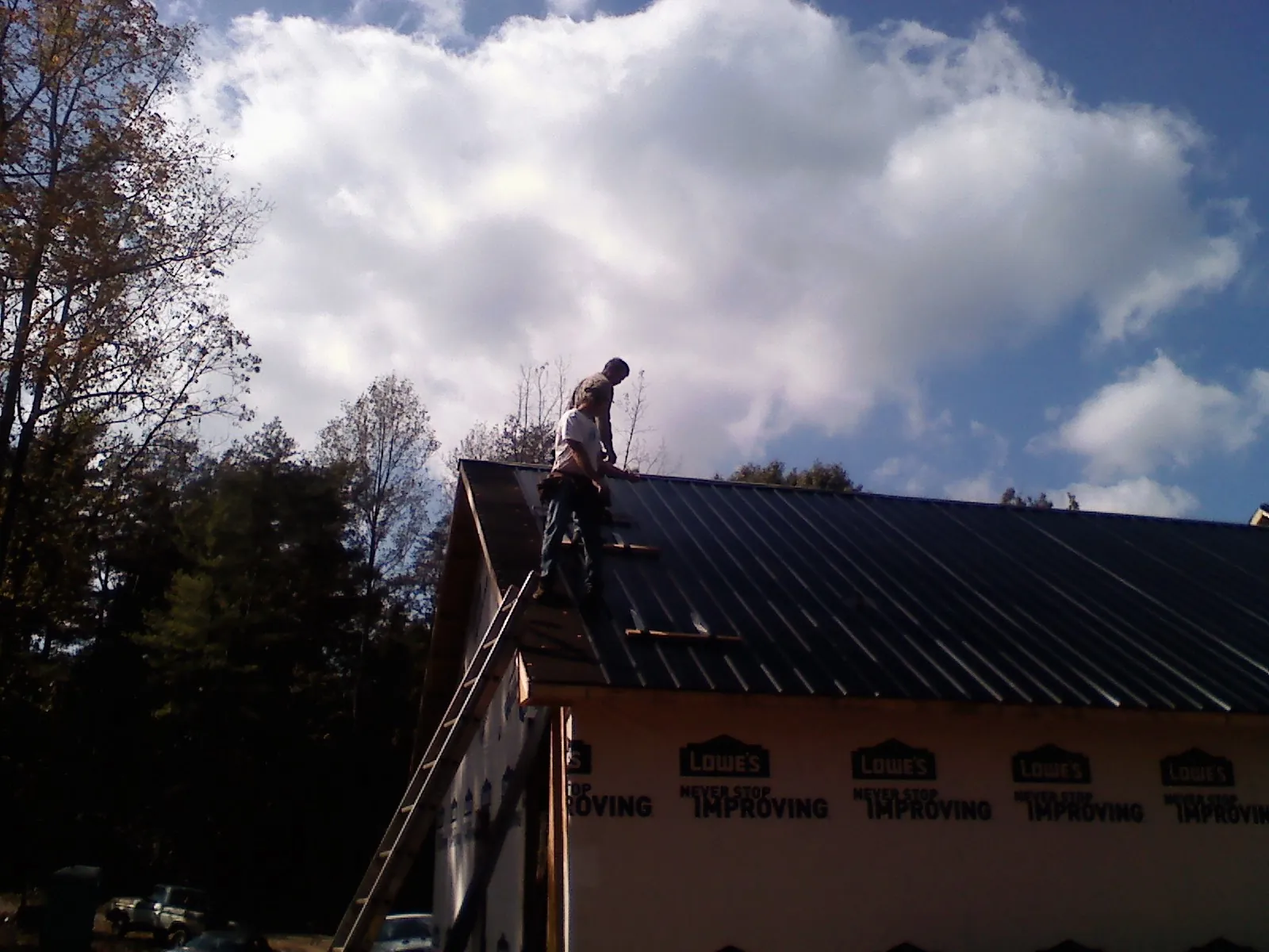 Roofer fastening dark metal panels high against a cloudy sky, from a Roof Inspection job in Ellisburg
