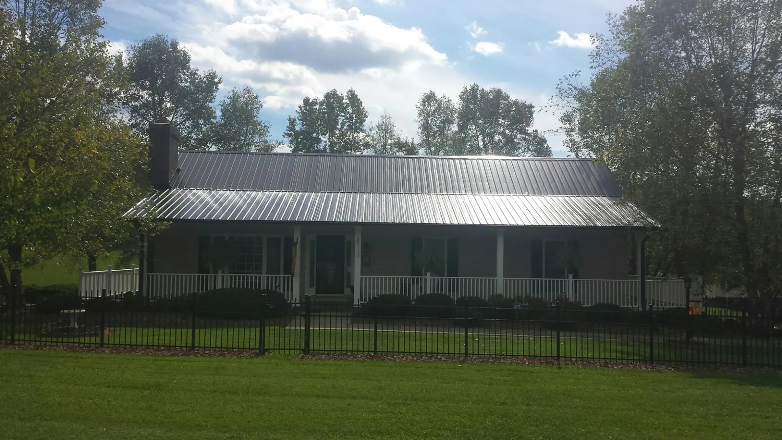 Gray metal roof on a brick ranch with a full width front porch — Gutter Guard Installation work by our crew in Ellisburg
