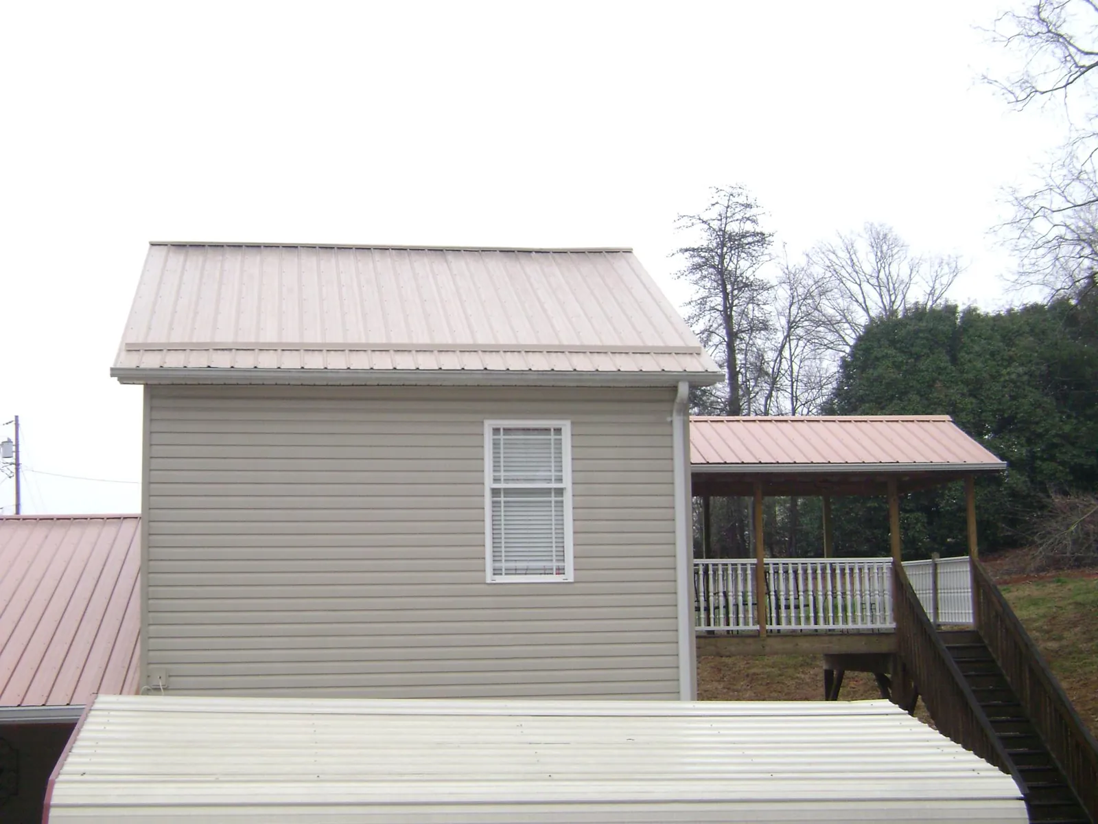 Tan metal roofs on a two story addition and attached porch, from a Roof Replacement job in Ellisburg